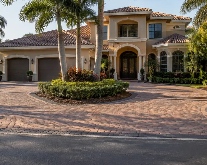 A circular driveway of tan and red blend pavers with a charcoal border in front of a two story house